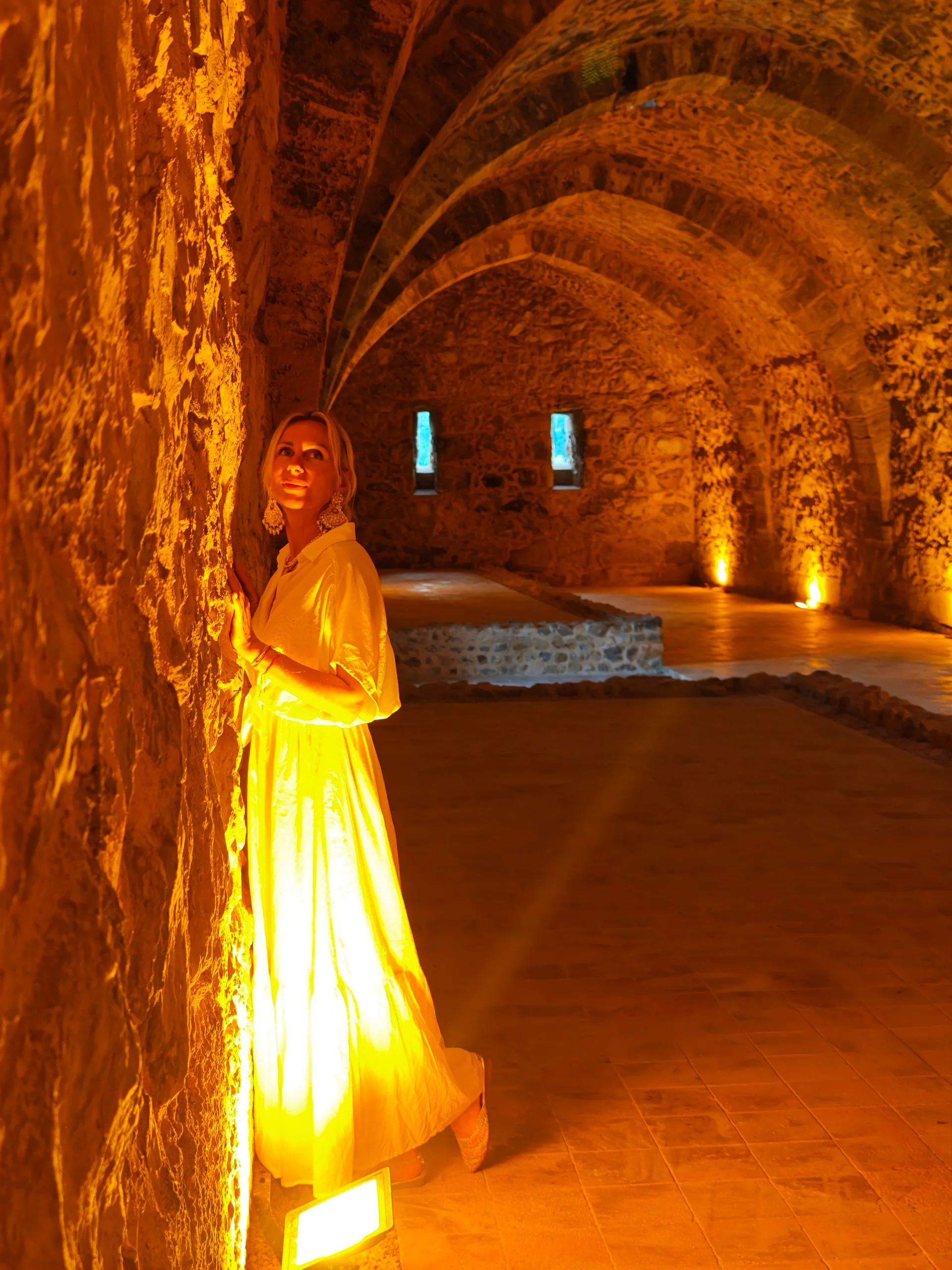 Woman in a white dress beneath warmly lit stone arches
